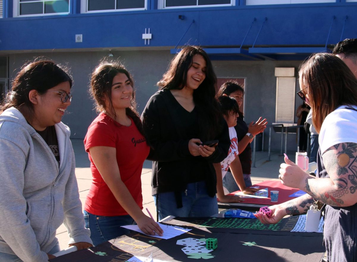 Give me a good one!
English teacher, Katelynn Beamish-Sanchez, Plays Areli Morales,9, Sofia Benavides, 9 and Liliana Agustin’s, 9, math night game. Beamish saw and played a variety of games at math night. “There was a lot of Plinko or bean bag toss and stuff like that but it was interesting that they were able to take games that are really similar and make them unique,” Beamish said. Additionally Beamish said she didn't know the students had to re-use poster boards because of how well the games turned out.
