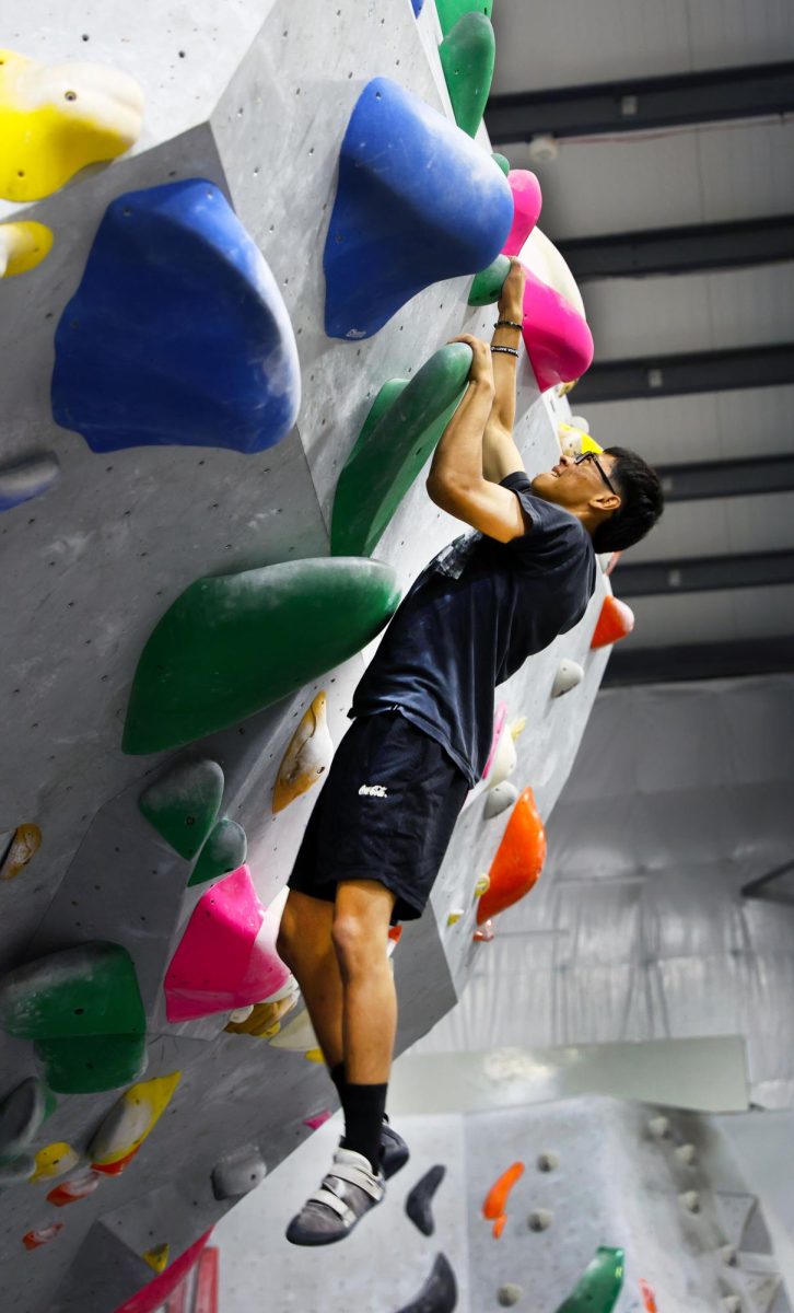 Rock solid. Gripping the plastic rock hold, David Villeda, 11, attempts to complete a bouldering route.  Villeda started rock climbing as a freshman, but had to take a break his sophomore year, due to injuries. He picked the sport back up with OG Outdoors Club, which took students to the Mesa Rim climbing gym once a week. “To me, this is really fun. I like climbing trees and buildings… It’s natural for me,” Villeda said. Villeda attempted a bouldering route, which was an unsupported style of climbing. Bouldering does not use a rope or harness and if climbers fall, they dropped to a padded surface below. The colored rocks on the wall represent the different routes, or paths, that climbers could take to reach the top. Photo by Noemy Melchor. 

