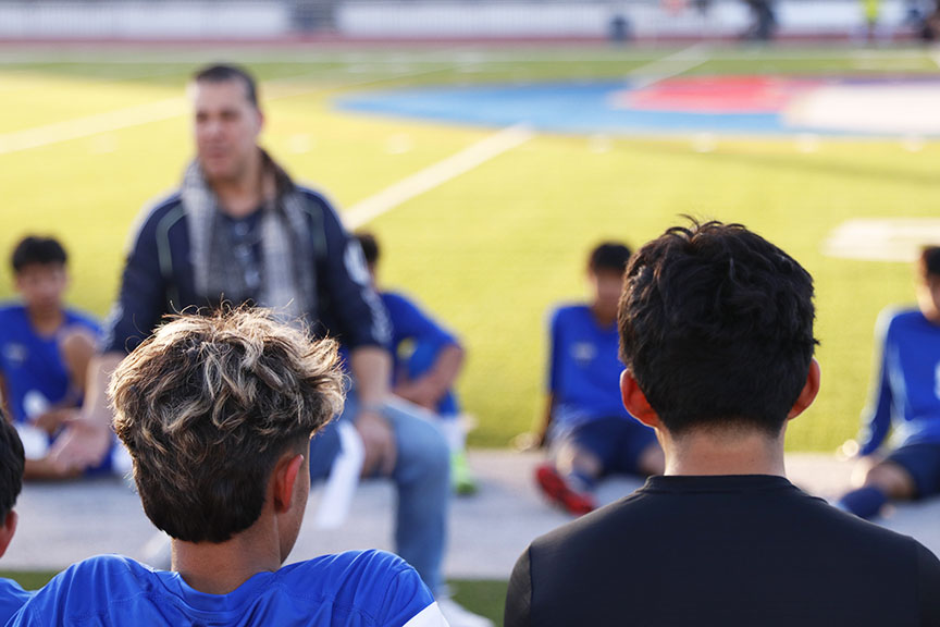 Group huddle! With the first half ending, Soccer Coach Roger Rolim calls in the JV Soccer players for a plan discussion for the next half of the game. The soccer players had struggled scoring a goal and needed to strategize a better plan. The coach represents a pattern the players need to follow in order to get across the field and shoot a goal. “After the meeting concluded, I felt more confident and ready to play,” Emmanuel Salvador, 11, said. The soccer players lost hope on winning this game. They lost more once Player Luis Martinez, 11, received an injury in the first half. Photo by Richie Martinez.
