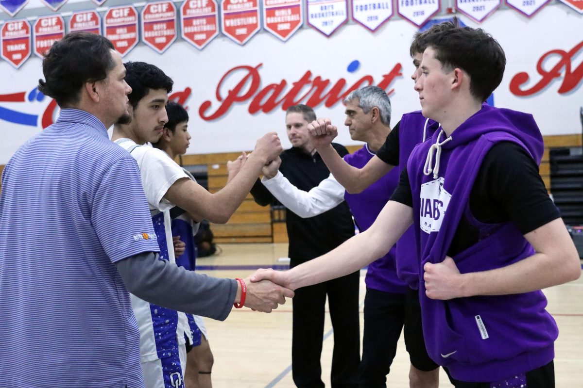 Let’s Play. Offering a handshake, Varsity Basketball Coach Roman Macias along with the team captains Andrew Martinez, 12 and Markus Maramba, 10, welcome the opposing team from Rock Academy. After each team completed their warm ups, the coaches and team captains greeted each other with handshakes and fist bumps. “My favorite part of playing basketball is meeting the people I go against,” Varsity player Jyan Allado, 10, said. Depending on who the team is playing against the coaches will make a game plan and concept for the players to follow throughout the game. Photo by Azul RiosChavez